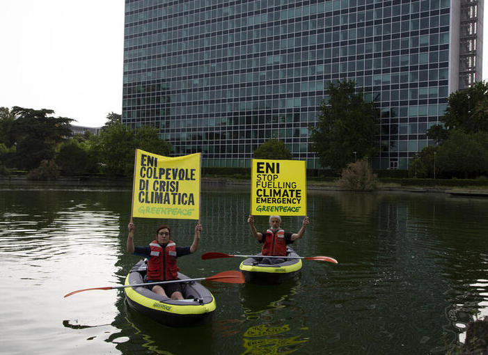 Two Greenpeace Italia activists sit in kayaks in front of energy company ENI headquarters, holding signs that say "Eni guilty of climate crisis" and "Eni stop fueling climate emergency"