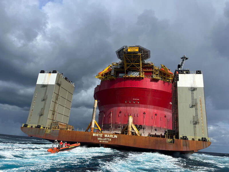 On the open ocean, a small, red inflatable boat of climate activists is dwarfed by the enormous offshore oil drilling platform that it is approaching.