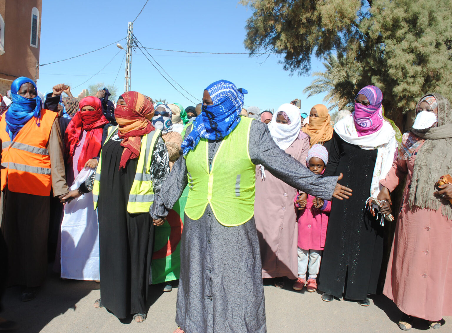 Women in colorful Muslim headscarves standing together on a street and holding hands
