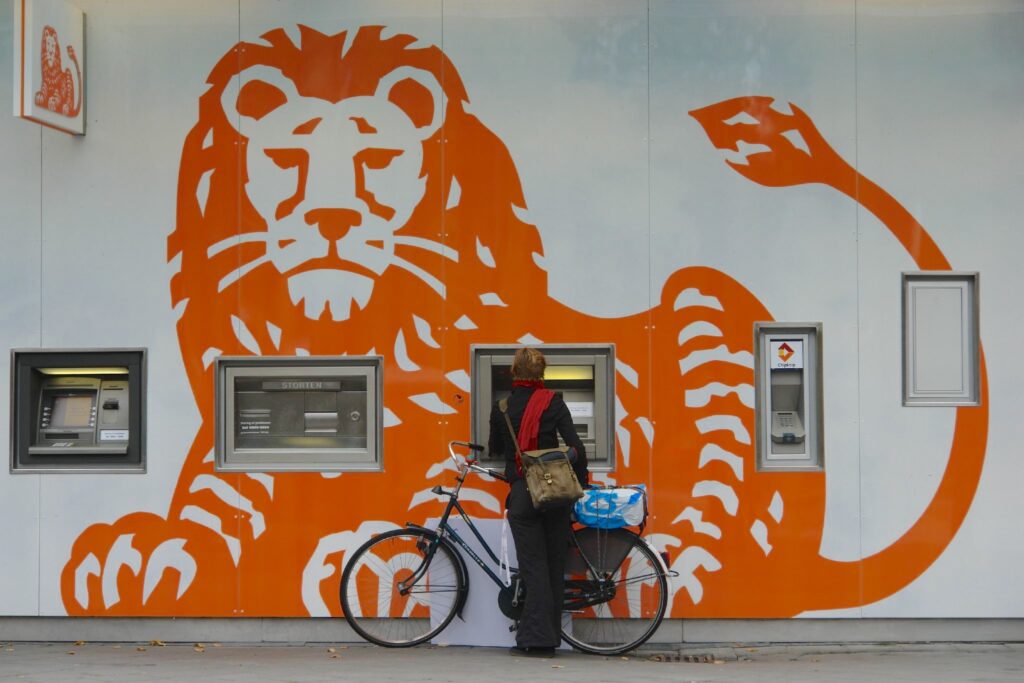 A woman with her bike at an ING bank ATM and the orange lion ING logo painted on the building wall.