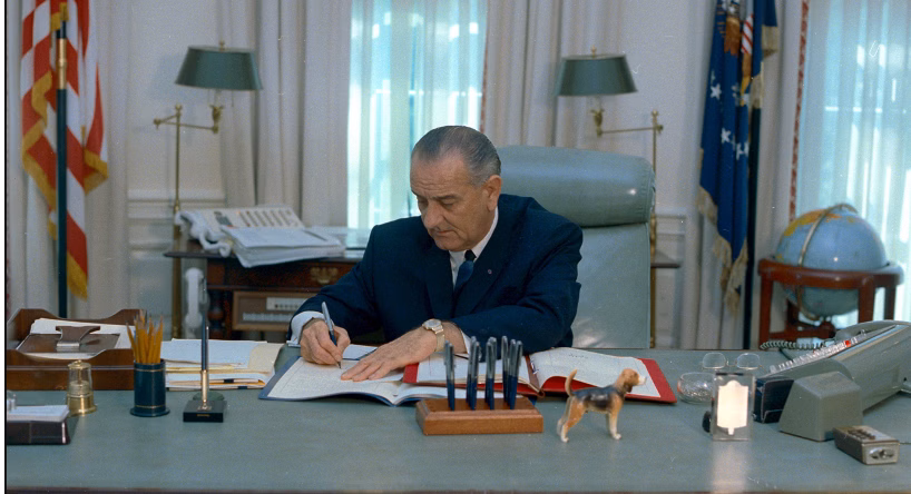 U.S. President Lyndon B. Johnson signs documents at a desk.