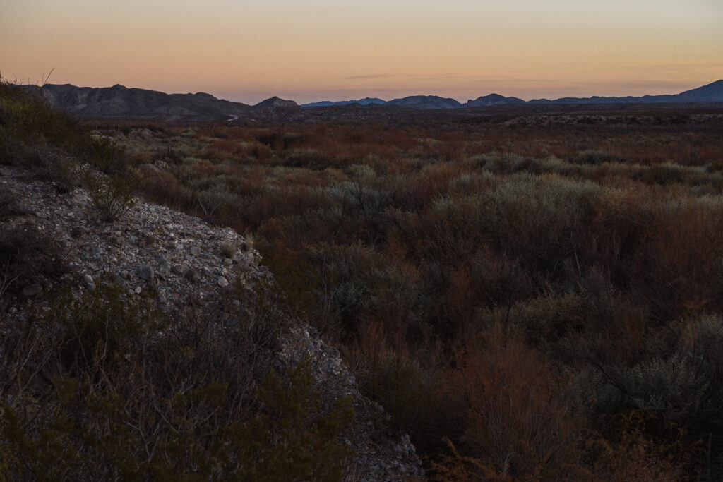 Orange and purple sky with the setting sun over the dusky green and buff of the Texas desert.