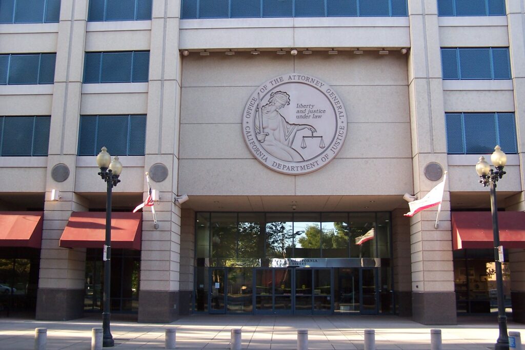 Outside view of beige office building with seal of Office of the Attorney General - California Department of Justice over the door.