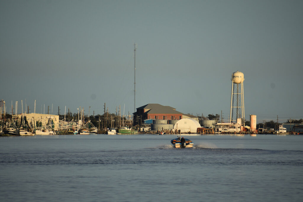 A view of Calcasieu River with a small boat, water tower, marina, and small buildings.