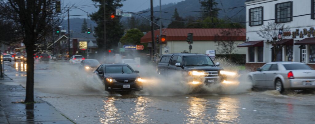 Cars spray water as they pass through a small city street.