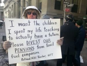 Woman holding protest sign that reads, i want the children i spent my life teaching to actually have a future. please divest our pensions from fossil fuel companies - retired nyc teacher, uft