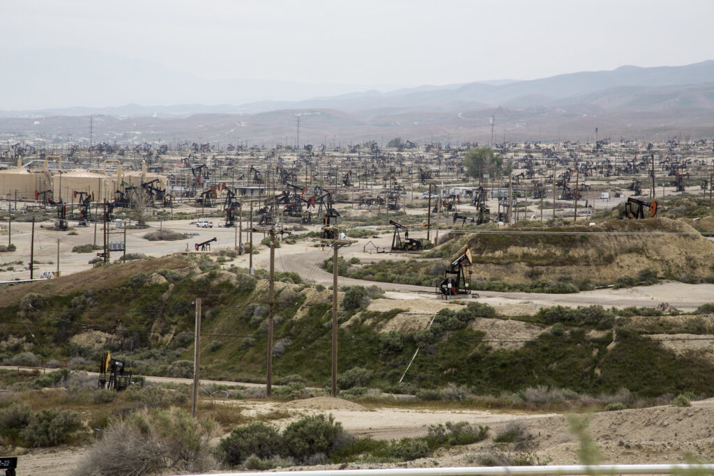 Oil and gas pumpjacks fill the California scrub landscape along a dusty road.