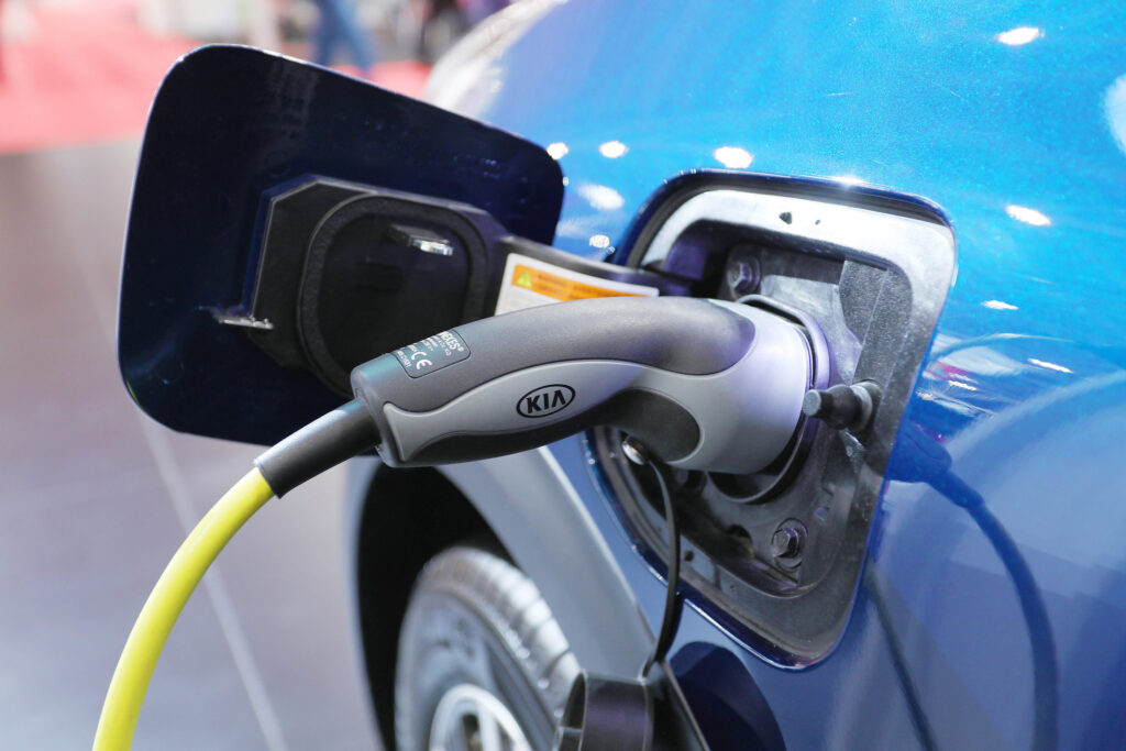 Close-up of Kia electric car charger with neon yellow cable plugged into a neon blue car.