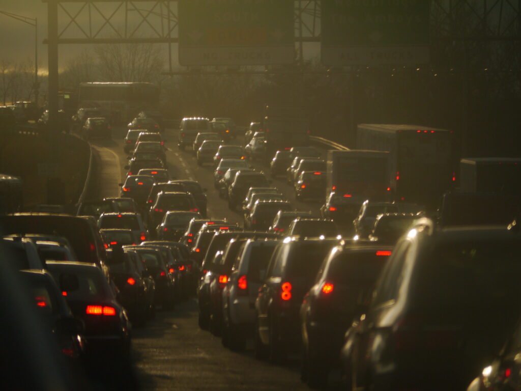 Dark smoggy rear view of four rows of cars and red tail lights sitting in traffic on the New Jersey Turnpike.