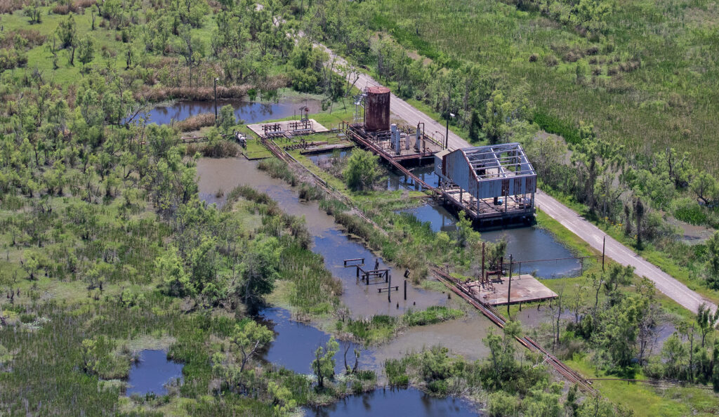 Rusted, flooded tanks and structures at an oil and gas well site amid marshland in Vermillion Parish, Louisiana.