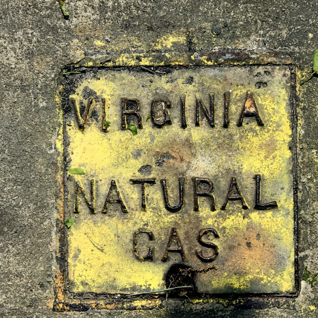 On cement, a metal utility cover painted yellow and reading 'VIRGINIA NATURAL GAS.'