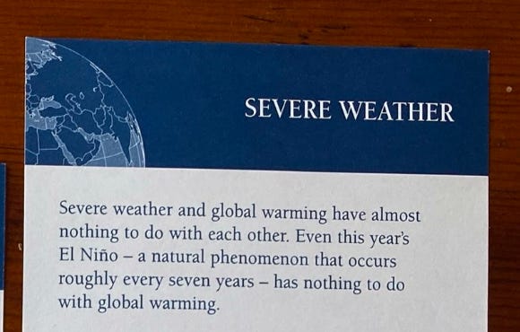 Blue and white folder on a mahogany table, with text 'SEVERE WEATHER: Extreme weather and global warming have almost nothing to do with each other. Even this year's El Nino - a natural phenomenon that occurs roughly every seven years - has nothing to do with global warming.'