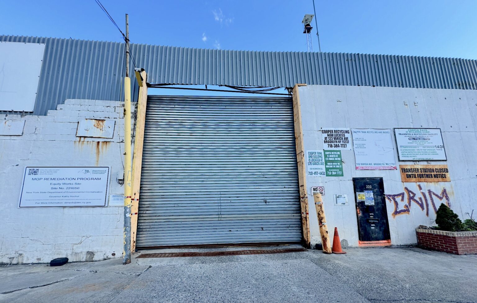 The gate to the Equity Works Gas Site in Brooklyn New York. Among several signed affixed to the dingy white brick walls on either side of the closed rolldown gate, one states it is in a state environmental remediation project.