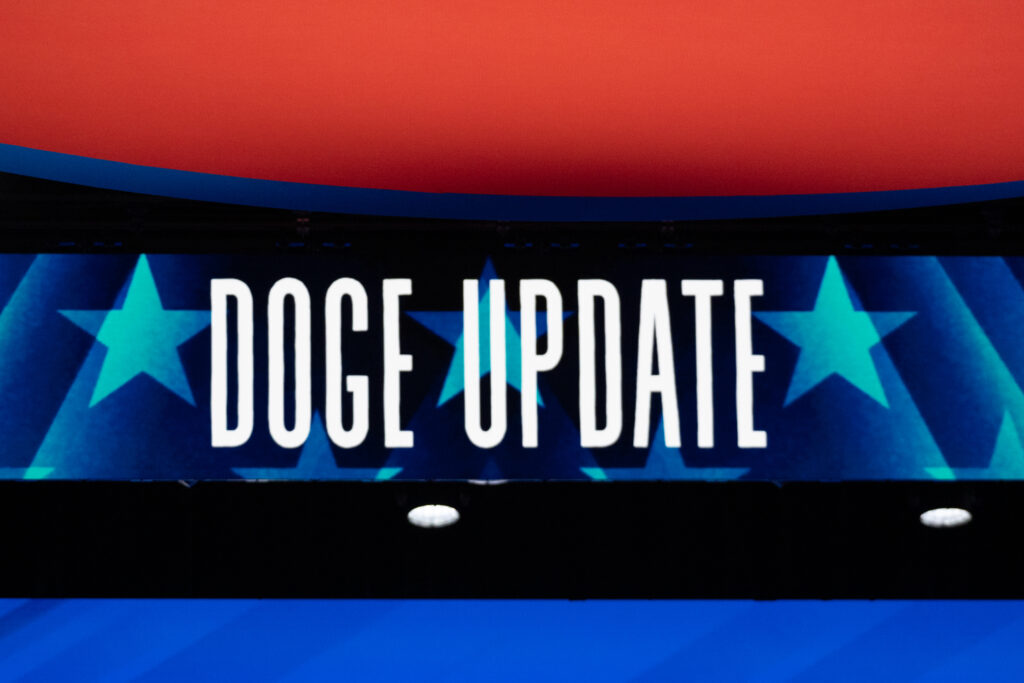 'DOGE UPDATE' projected in white letters on a dark background with teal stars and red stripe above and blue stripe below.