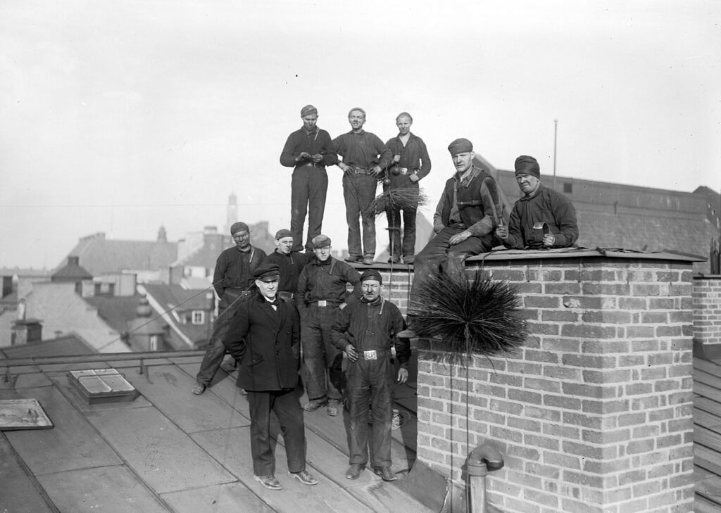 Ten chimney sweeps stand on a roof in 1905.