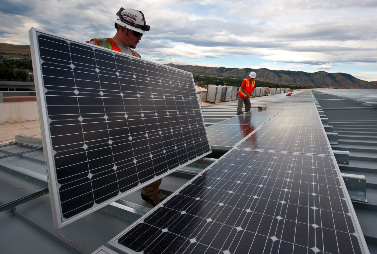 Two construction workers install solar panels.