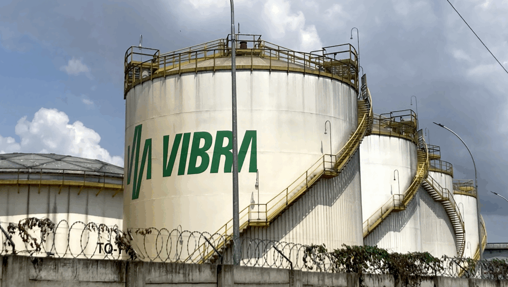 A line of giant white fuel silos, one behind the other receding to the right. The Vibra logo painted in green is visible on the front silo.