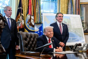 President Donald Trump, flanked by Secretary of Energy Chris Wright and Secretary of the Interior Doug Burgum, signs an Executive Order approving the Ambler Road Project in Alaska, Monday, October 6, 2025, in the Oval Office.