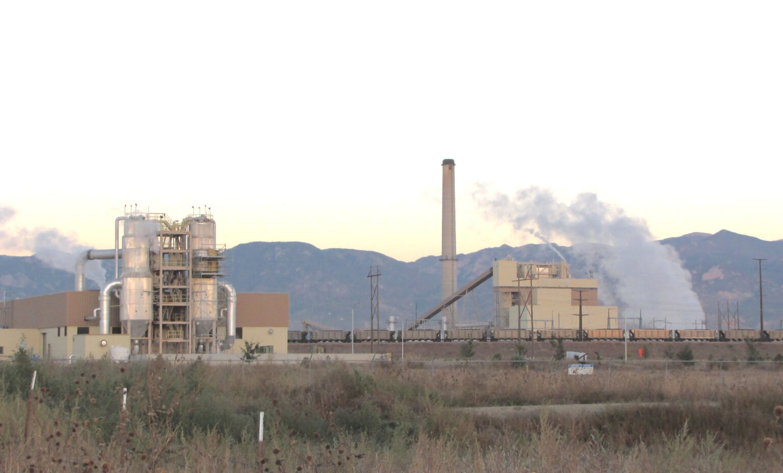 A coal-fired power plant with white emissions visible and rounded mountains in the background.