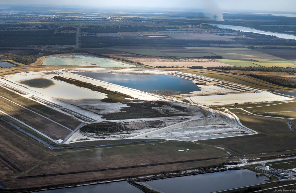 Mosaic Fertilizer's mound at the Uncle Sam plant in Convent, LA in the 4th District of St. James Parish. The company stores gypsum waste containing acidic and radioactive materials there, and smoke from sugarcane fields set ablaze is visible in the distance. The gypsum site was in danger of collapsing in 2019, threatening to contaminate waterways nearby.
