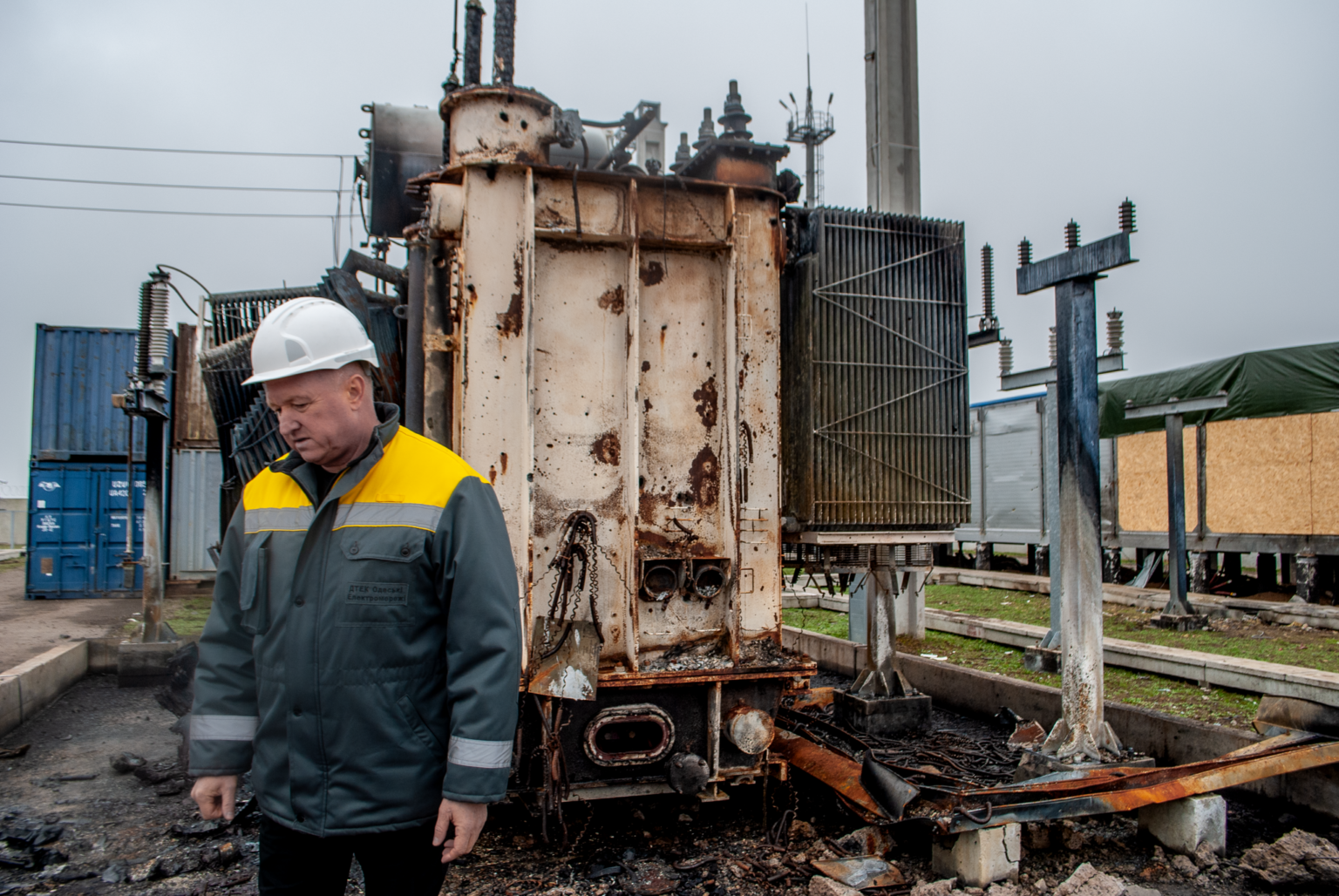 A utility worker in a hard hat, left, stands beside a transformer destroyed by a Russian drone near Odessa, Ukraine.