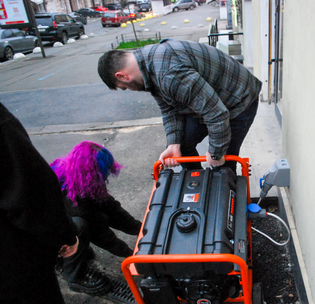 Dasha with bright purple hair, left, and a passing stranger try to start a cafe's generator on the sidewalk during a blackout in Kyiv. 