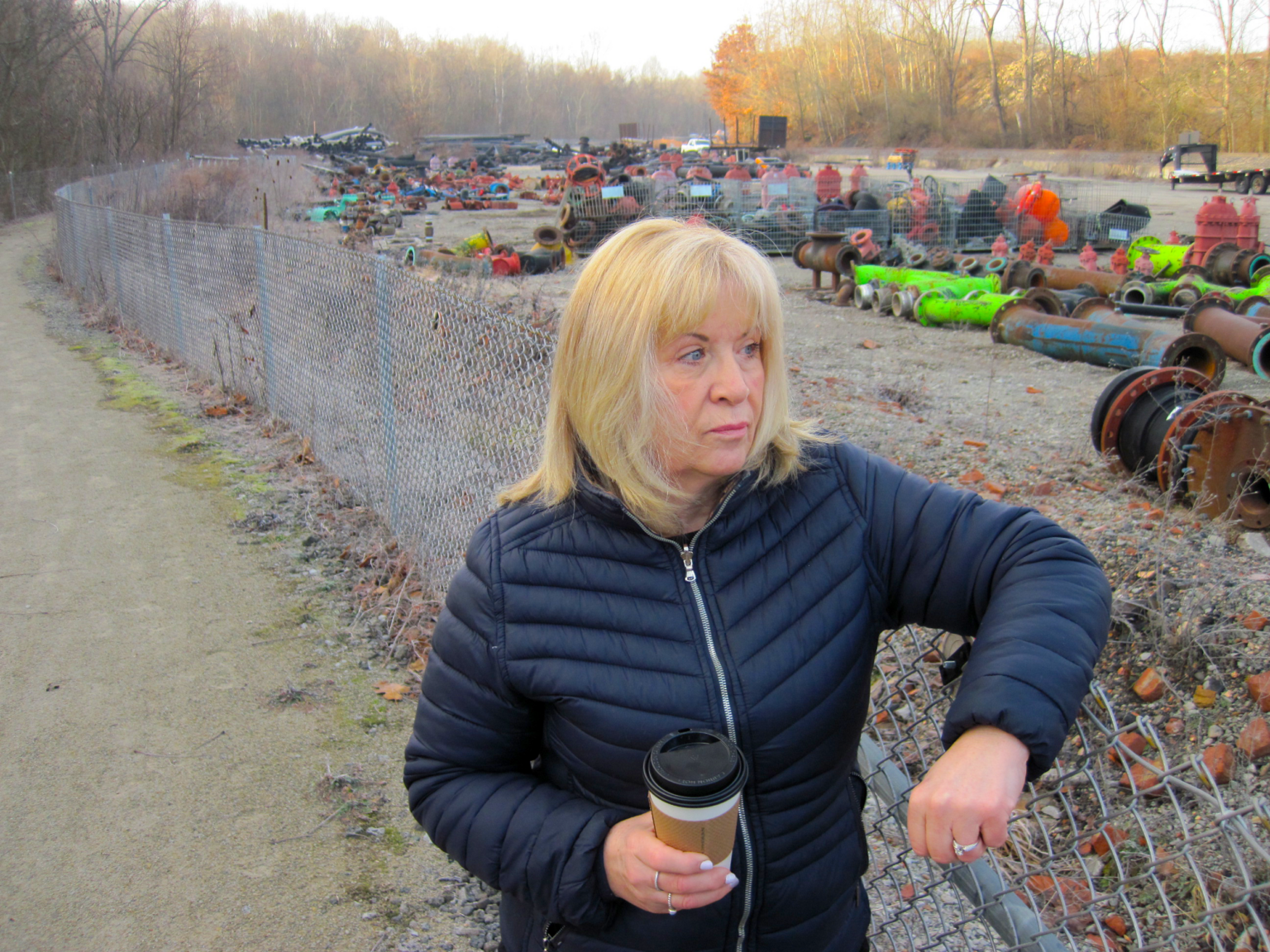 Janice Blanock leaning on the fence dividing a running and biking trail from the Cecil oil and gas waste yard.