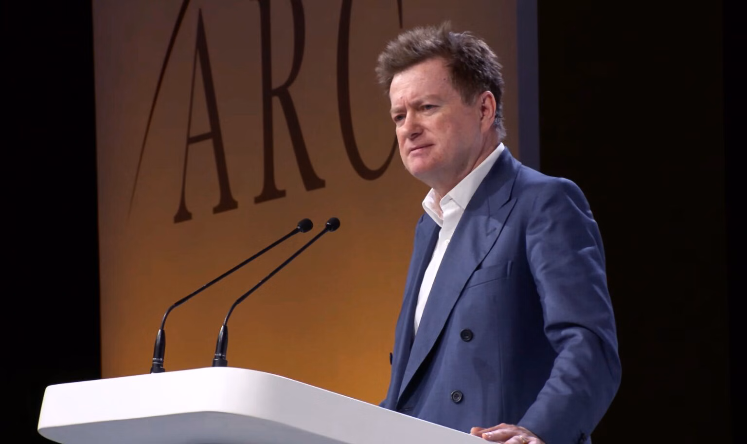Paul Marshall stands at a podium, with 'ARC' on the wall behind him.