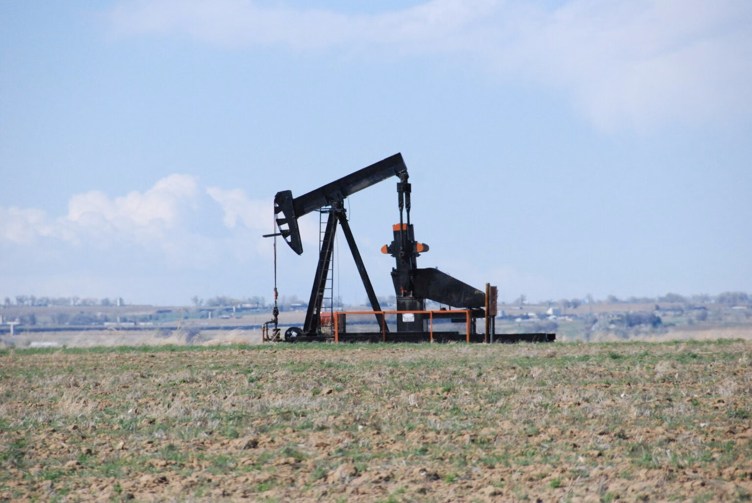 An oil pumpjack in an arid field tinged green under a blue sky in Colorado.