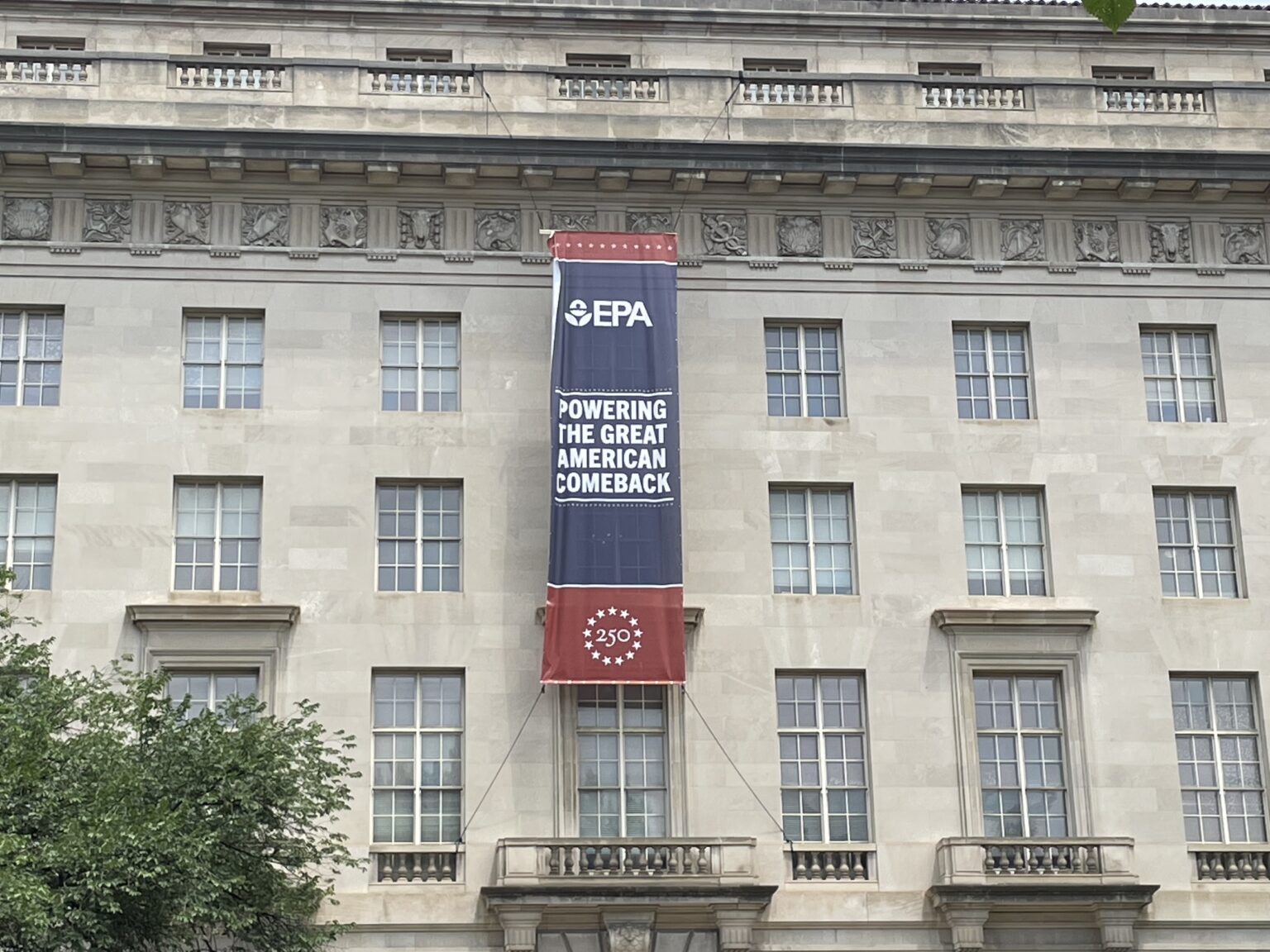 A red, white, and blue banner with the EPA logo and U.S. 250th anniversary that reads 'Powering the Great American Comeback' on the outside of the EPA headquarters in Washington, D.C.