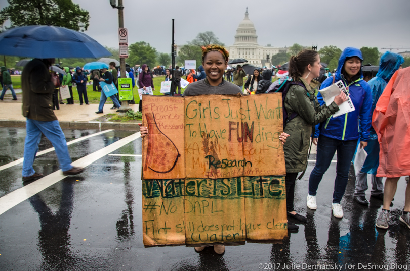Ivory Dean holds her sign in the rain saying 'Girls just wanna have FUNding. Asking me about my research.'