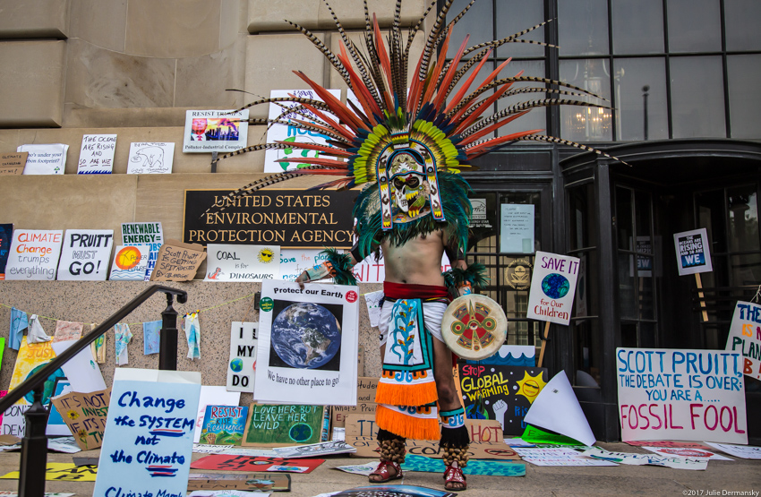 Member of an Aztec dance group with signs from the People's Climate March in front of the EPA's office in DC