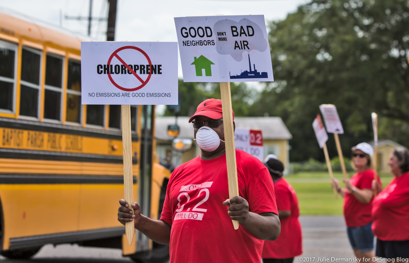A man in a red t-shirt and medical mask holds signs about air pollution