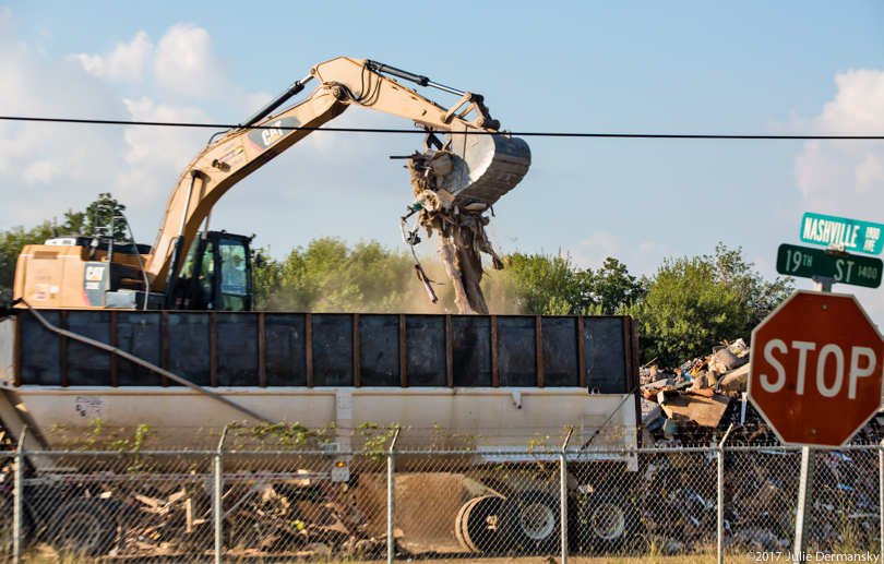 An excavator at the storm debris dump kicks up dust