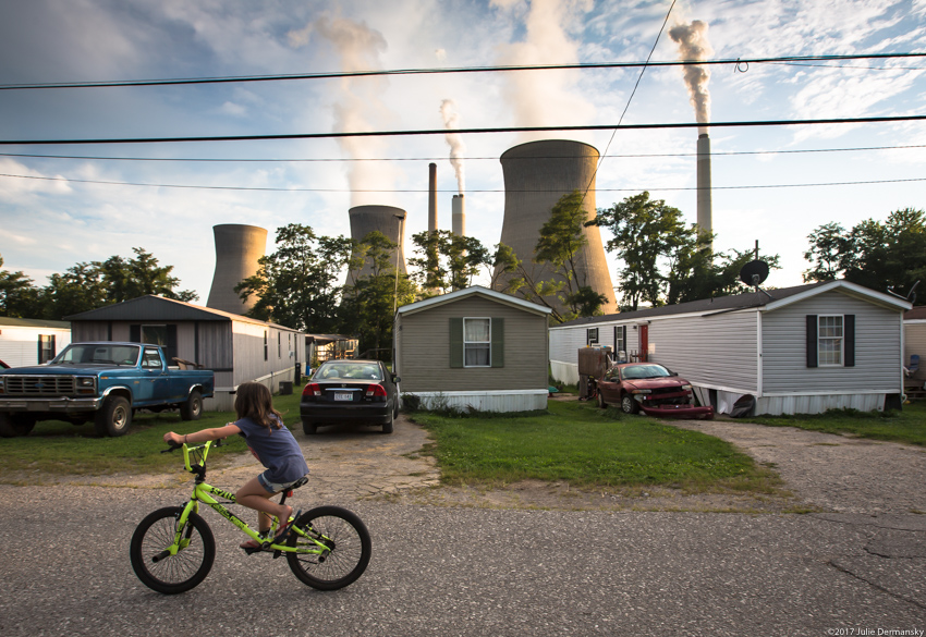 A girl rides her bike past trailer homes and the John Amos coal plant in Raymond, West Virginia.