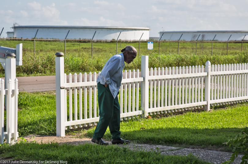 A woman of St. James Parish in her yard, with oil tanks in the background