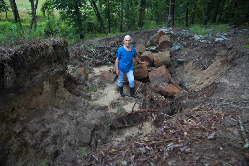Texas landowner Eleanor Fairchild stands in a deeply eroded cut on her land.