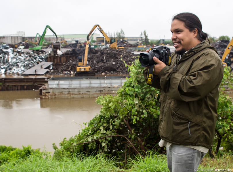 Bryan Parras takes a photo across the water from heavy machinery at a recycling facility in Houston