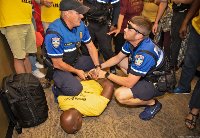 Pastor Gregory Manning with Justice and Beyond being pinned to the floor by police officers during a protest outside the Louisiana Association of Business and Industry office in Baton Rouge.