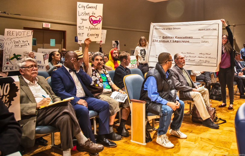 Many in the crowd at a New Orlean city council utility committee meeting hold signs protesting the Entergy gas plant