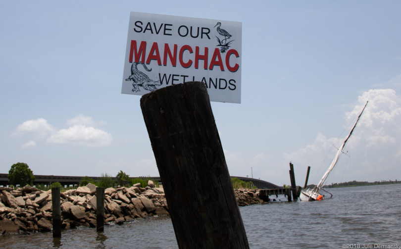 Save Our Manchac sign in front of a damaged sailboat tied to a boat launch