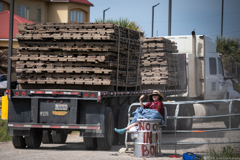 Truck loaded with mats passes next to protester chained to a barrel in the road