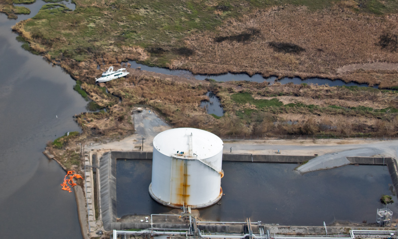 Boat stranded in marsh next to an oil and gas storage tank near Westlake, Louisiana.