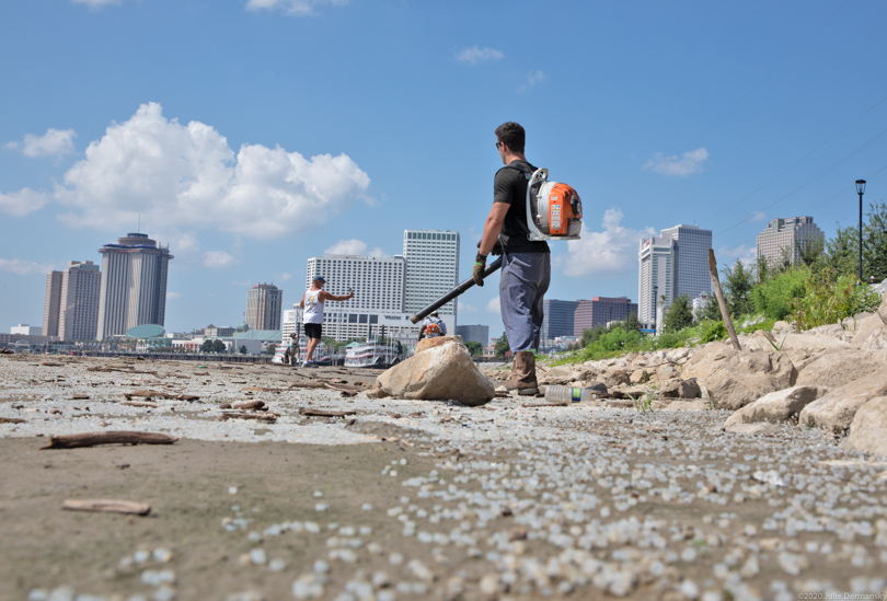 Cleanup workers using leaf blowers to collect nurdles on a New Orleans river bank