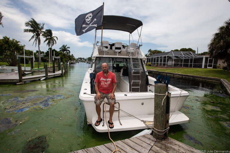 Juergen Kreuzer sits on the end of his boat with pirate flags in an algae-filled canal in Cape Coral, Florida.