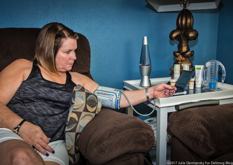 A white woman sitting down measures her blood pressure and pulse at home