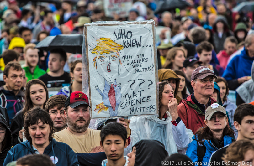 Man holding sign making fun of Trump's climate science denial.