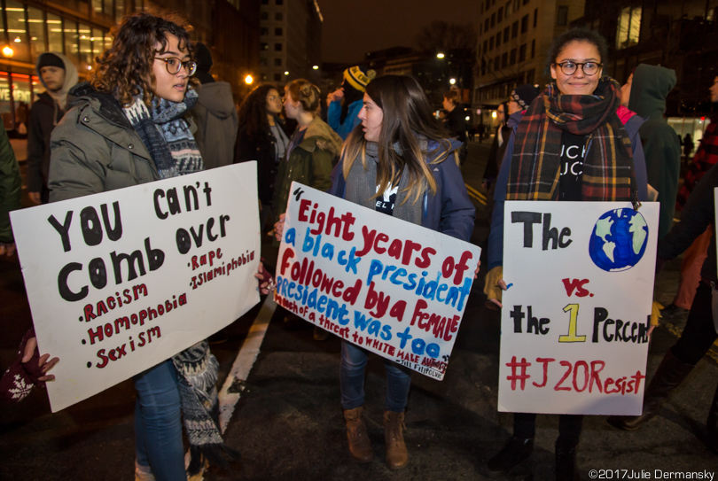 Protesters hold signs against racism, sexism, homophobia, and more.