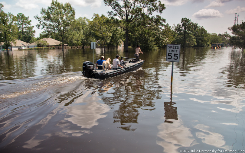 People and a dog in a motor boat navigate the flooded streets of Vidor, Texas