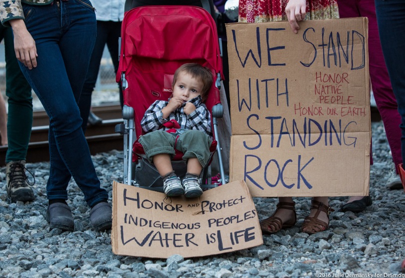 A child sits next to signs in support of the Standing Rock Sioux Tribe.